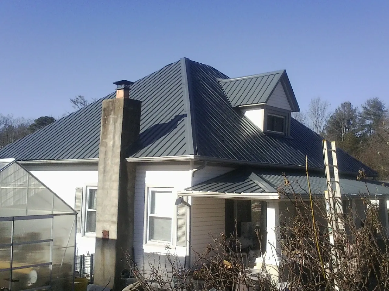 Dark blue standing seam metal roof on a white farmhouse with dormer — Slate & Tile Roof Repair by Roofing Brothers in Valley Stream