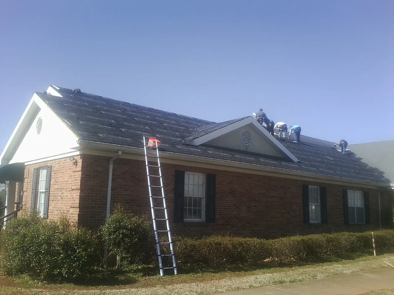 Crew tearing shingles off a brick ranch roof with a ladder set — Emergency Roof Repair work by our crew in Valley Stream