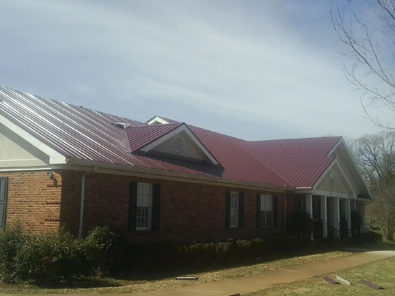 Red metal roof with gabled entries on a long brick building, from a Hail Damage Roof Repair job in Valley Stream