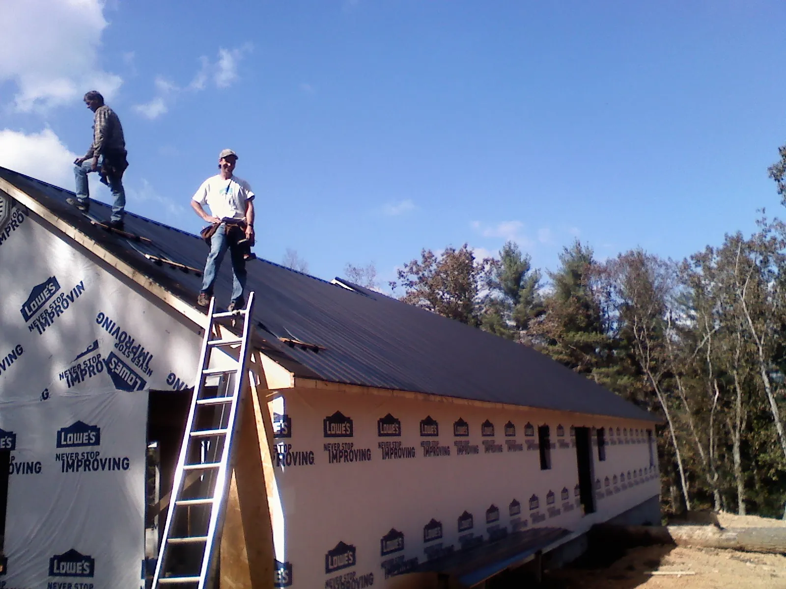 Two roofers standing on a long dark metal roof over a wrapped building in Valley Stream