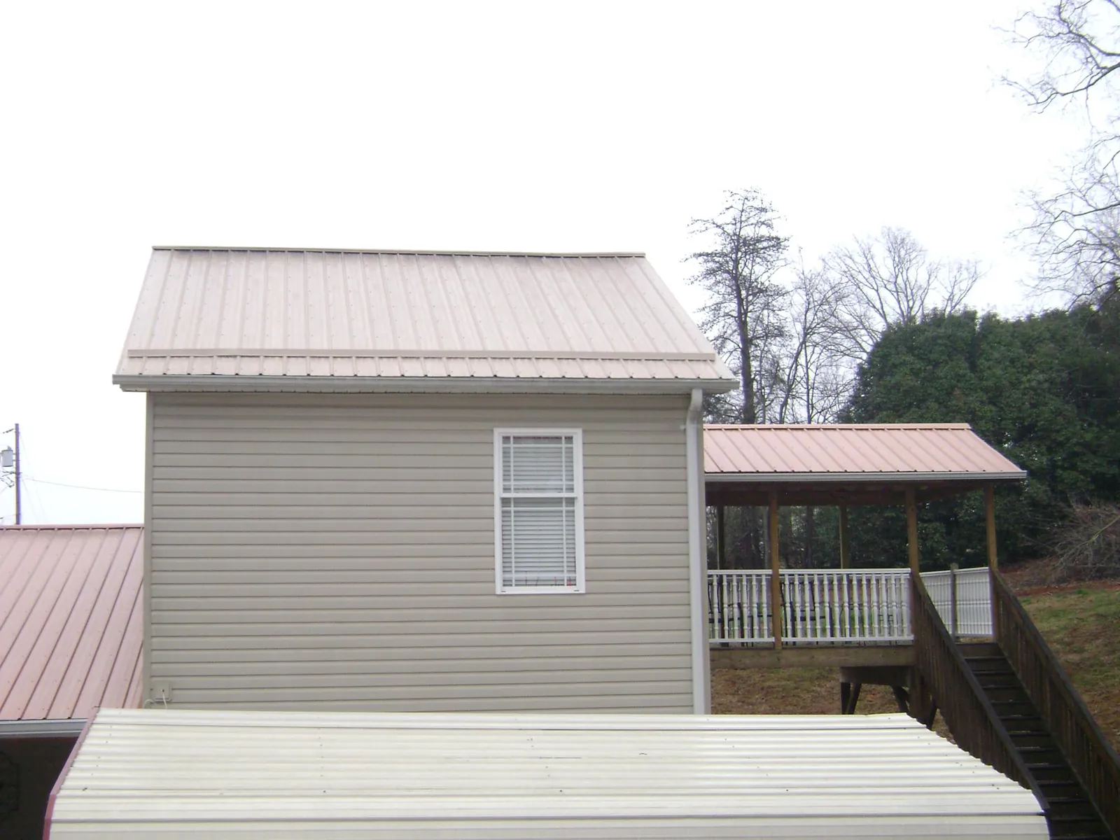 Tan metal roofs on a two story addition and attached porch, from a Roof Replacement job in Valley Stream